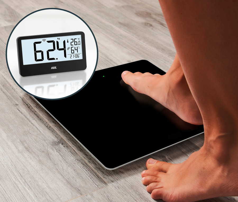 Barfuß auf einer schwarzen digitalen Personenwaage stehend, die 62,4 kg anzeigt.