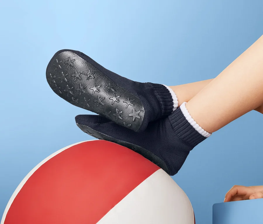 Füße in Strand- und Sportsocken ruhen auf einem Strandball vor blauem Hintergrund.