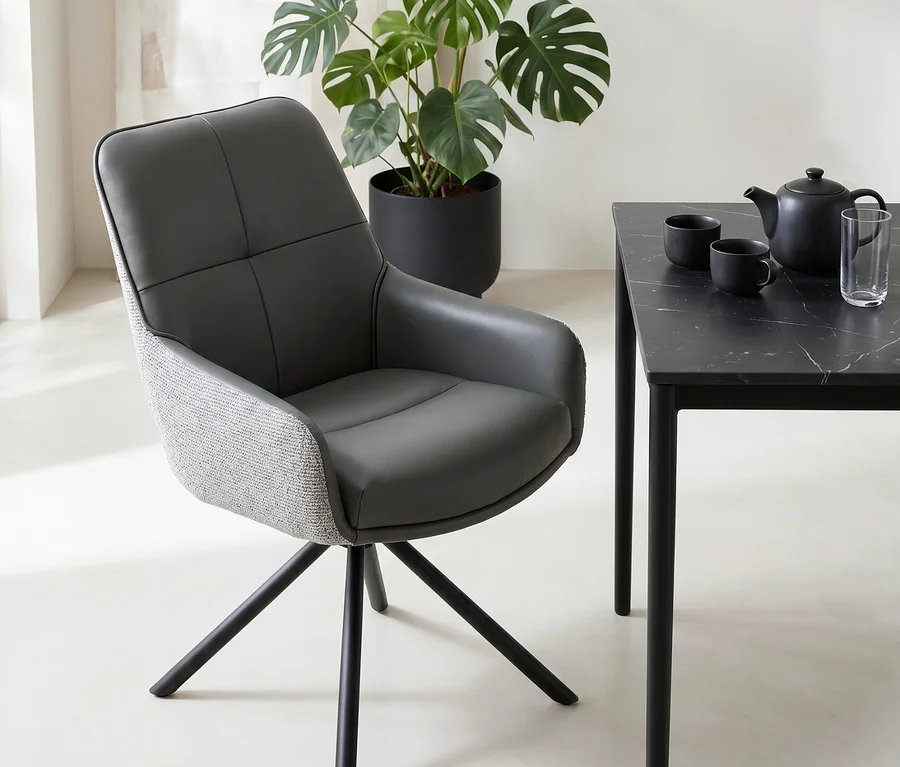 Ein modernes Zimmer mit einem dunkelgrauen Stuhl, einem schwarzen Tisch mit Marmorplatte, einer Teekanne und Tassen sowie einer großen Monstera-Pflanze in einem schwarzen Topf.