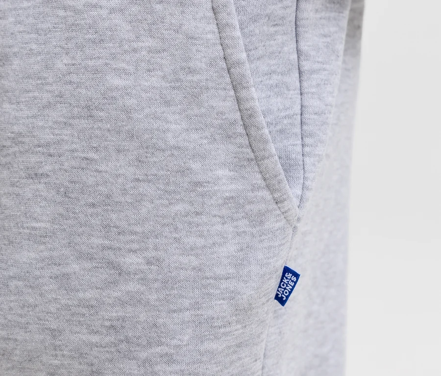 Nahaufnahme einer grauen Jack&Jones Bradley Sweatpants, die Stofftextur, eine Seitentasche und ein blaues Jack&Jones Etikett zeigt.
