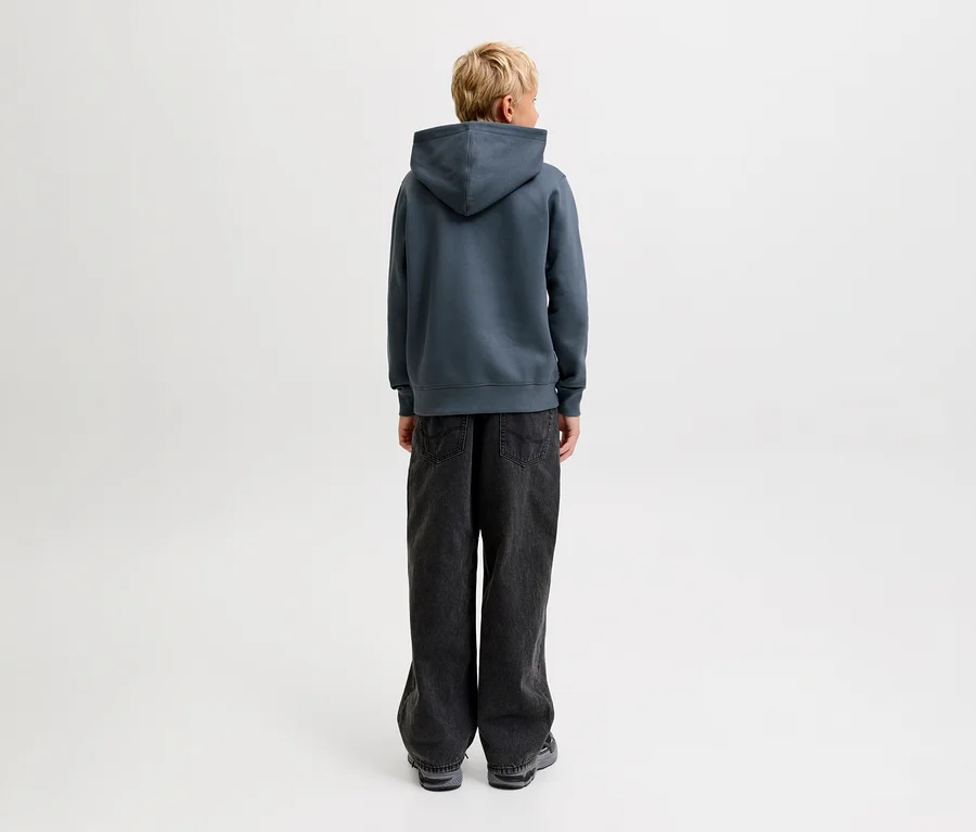 Person mit blondem Haar, von hinten gesehen, trägt einen dunkelgrauen Jack&Jones Star Sweat-Hoodie und dunkle, weit geschnittene Jeans.