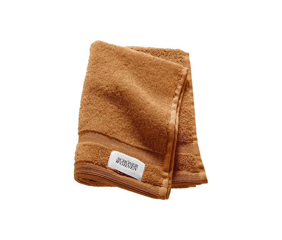 Ein gefaltetes braunes Gästehandtuch der SCHÖNER WOHNEN-Kollektion »Cuddly« mit weißem Etikett.