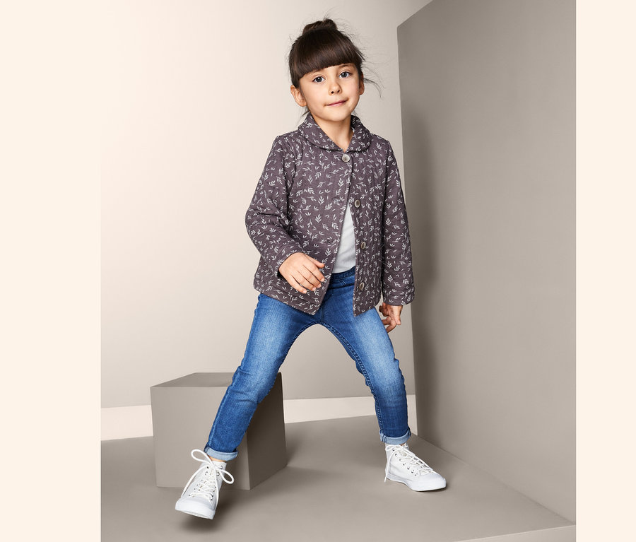 Mädchen posiert in Baumwoll-Steppjacke, Jeans und Turnschuhen.