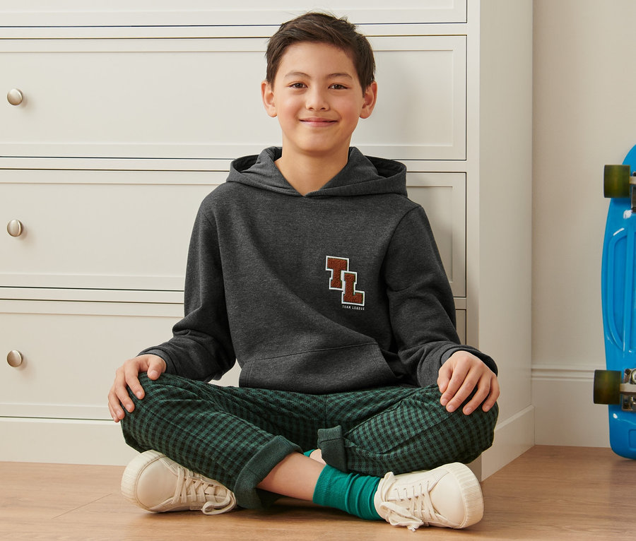 Junge sitzt mit Sweat-Hoodie auf dem Boden.