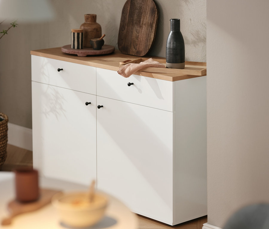 Auf einer weißen Kommode stehen ein braunes Holzbrett und diverse Dekoartikel. Darüber hängt eine Design for the people by Nordlux Hängeleuchte »Strap 16«.