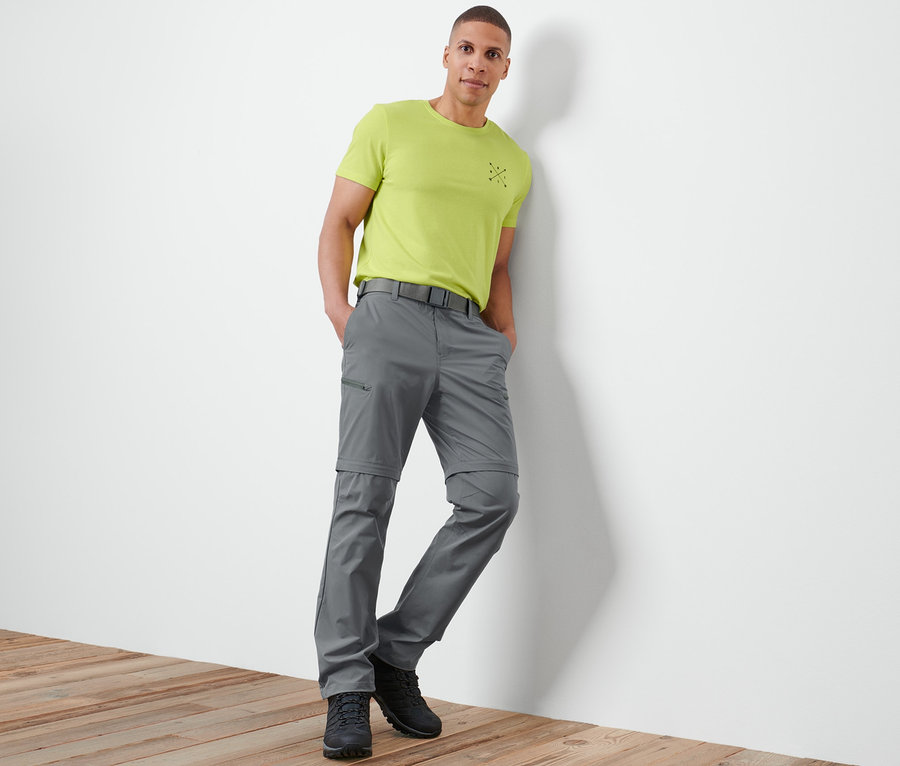 Mann lehnt an Wand, trägt graue 2-in-1-Funktionshose.