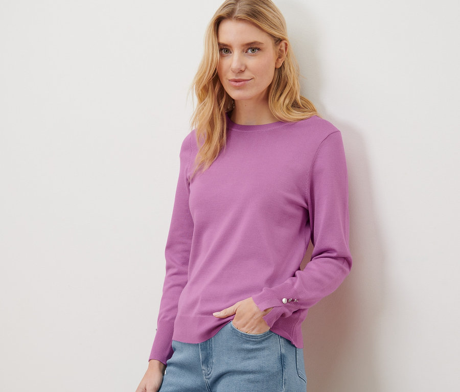 Frau posiert in einem rosa Feinstrickpullover und blauen Jeans.