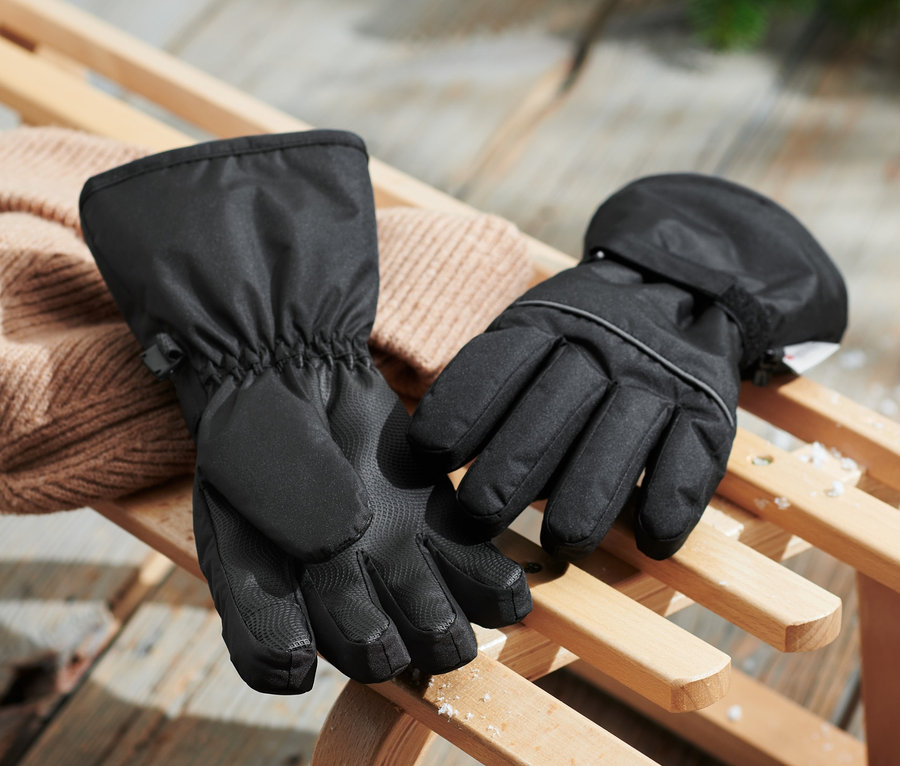 Schwarze Kinder-Ski- und Winterhandschuhe liegen auf einem Holzschlitten neben einer beigen Strickmütze.