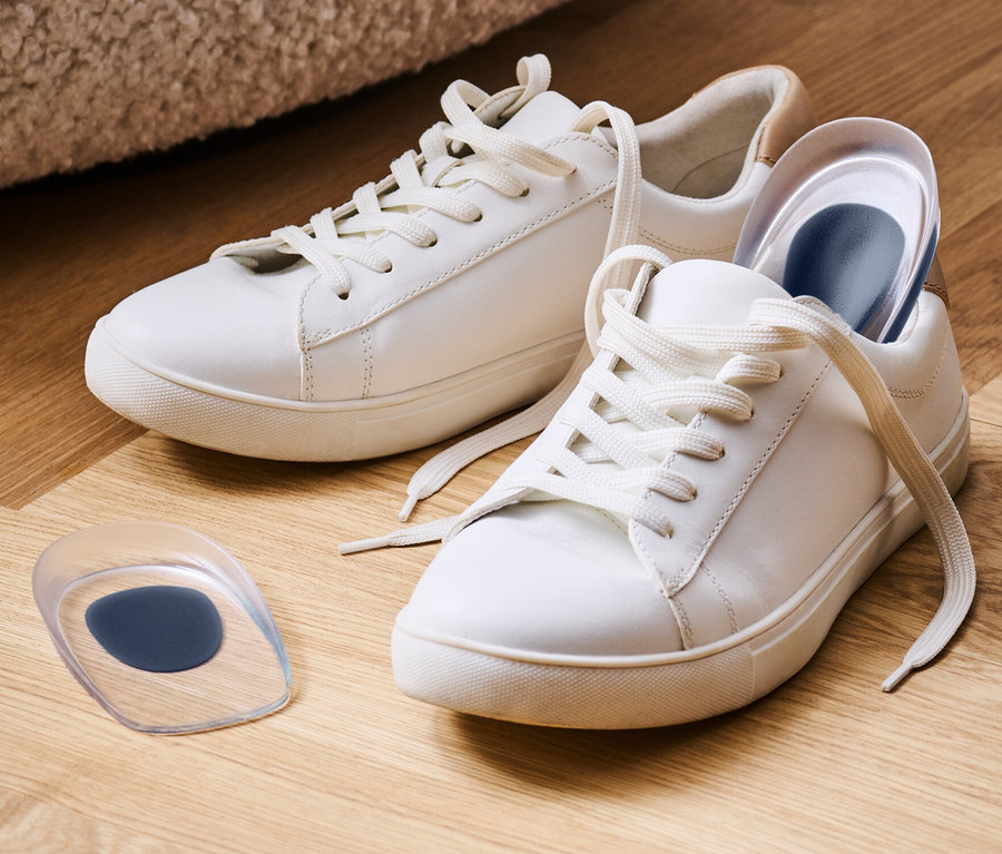 Zwei weiße Turnschuhe mit je einem Paar Fersenkeile auf einem Holzboden.