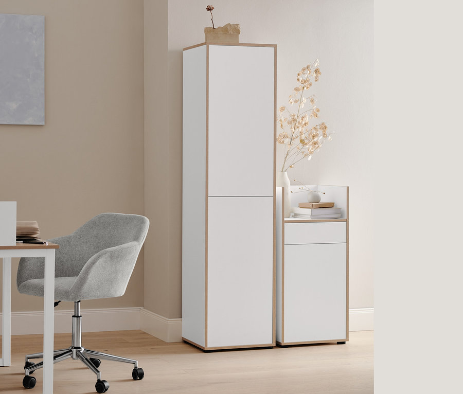 Ein beiger Schreibtischstuhl steht an einem weißen Sekretär mit seitlicher Umrandung. Daneben stehen ein hoher und ein kleiner Büroschrank mit Furnierkante. Auf dem Tisch steht eine Tischleuchte aus Metall.