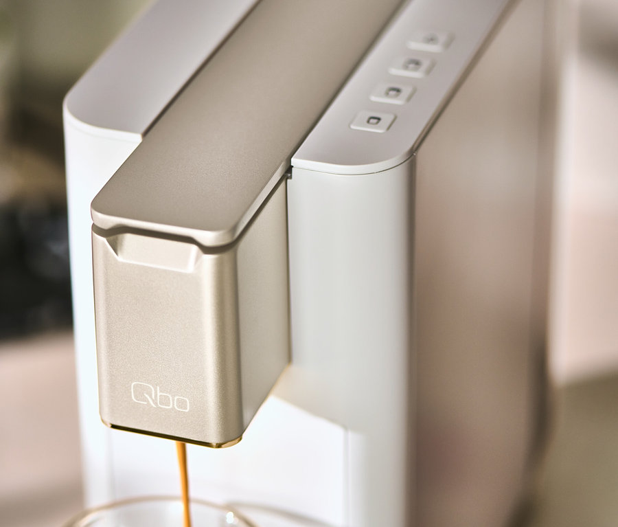 Eine Qbo ICONIC Light Gold Kaffeemaschine füllt eine Tasse mit Kaffee.