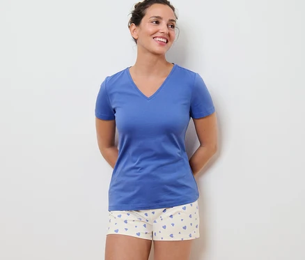 Frau trägt einen Shorty-Pyjama mit Herzen und ein blaues T-Shirt.