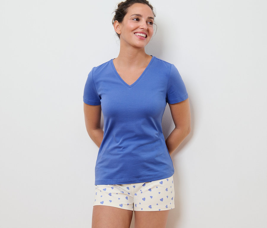 Frau trägt einen Shorty-Pyjama mit Herzen und ein blaues T-Shirt.