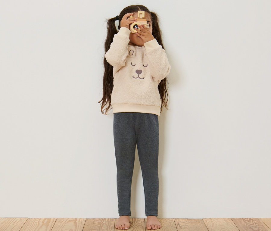 Mädchen schaut durch eine Holzkamera und trägt graue Kinder-Thermoleggings.