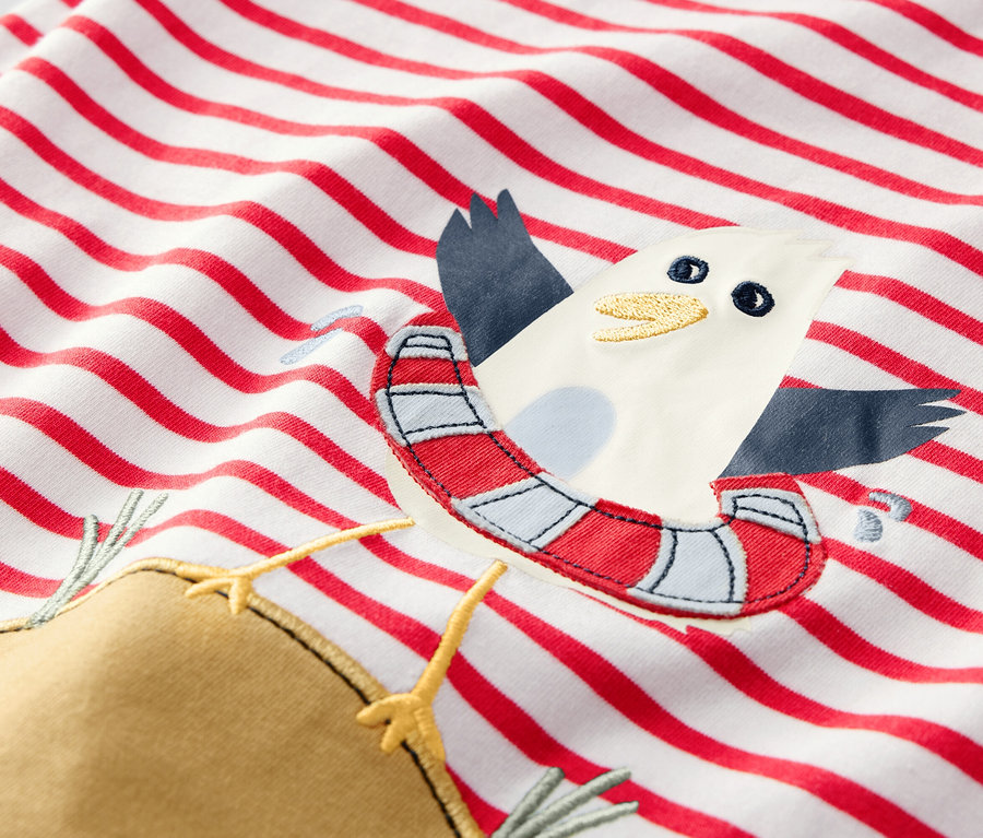 Detail eines Kinder-T-Shirts mit roten Streifen und einer Applikation einer Möwe mit Schwimmreifen.
