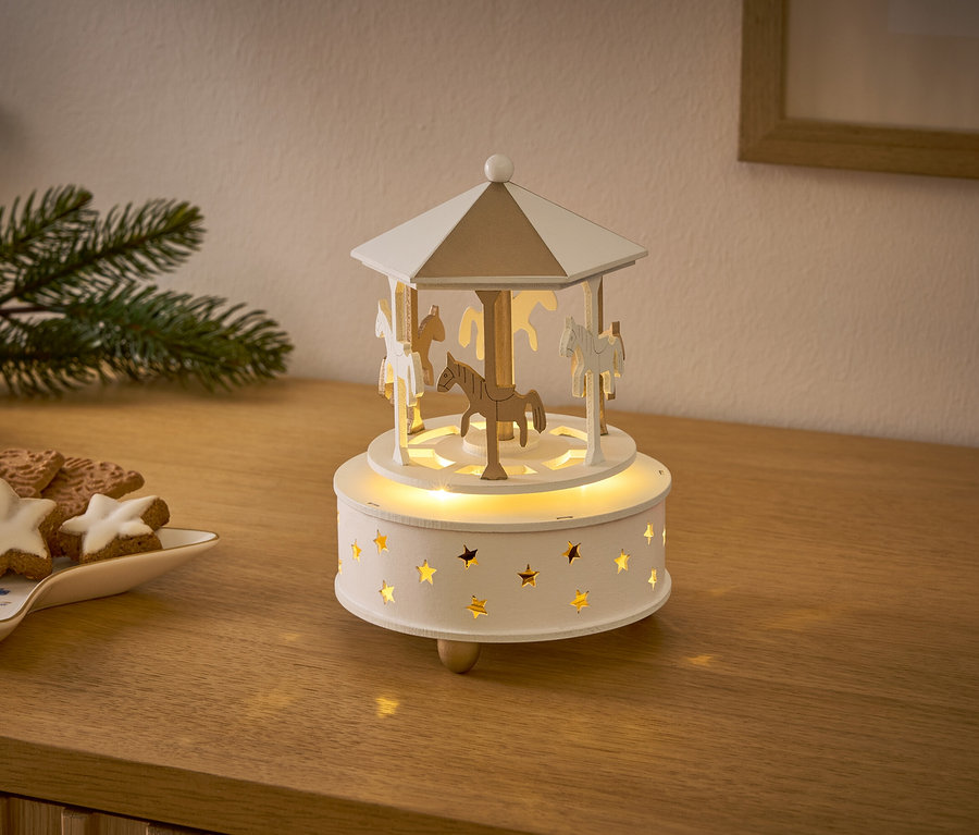 Ein hölzernes Karussell mit Pferden und Sternen leuchtet auf einem Holztisch neben Weihnachtsplätzchen.