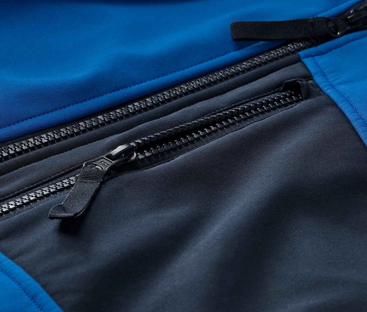 Detailansicht einer blau-schwarzen Softshelljacke mit Reißverschlüssen.