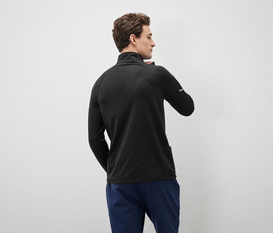 Mann in schwarzem Reißverschluss-Sweater und blauen Hosen, der nach links schaut.