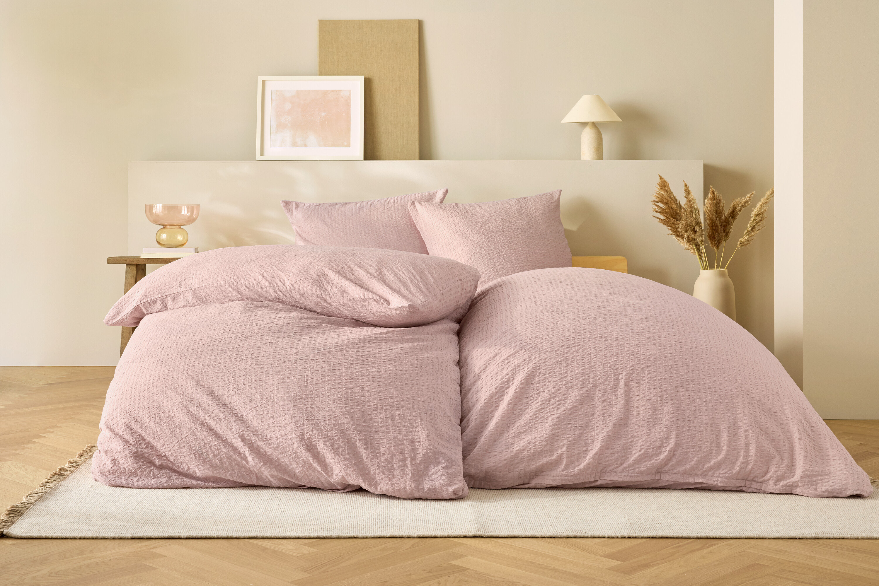 Rosa Bettwäsche auf einem Bett vor beigem Hintergrund.