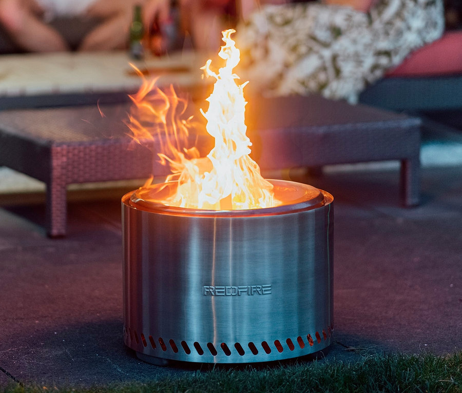 Silberfarbene RedFire Feuerschale »Volcano Extra Large« mit Feuer, im Hintergrund sitzende Personen.
