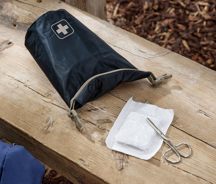 Eine geöffnete Erste-Hilfe-Tasche, eine Bandage und eine Schere liegen auf einer Holzbank.