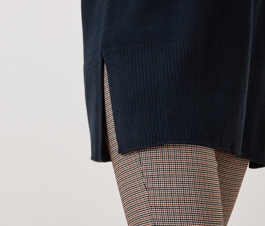 Detail eines Damenoutfits mit einem dunkelblauen Pullover mit Schlitz und einer karierten Hose.