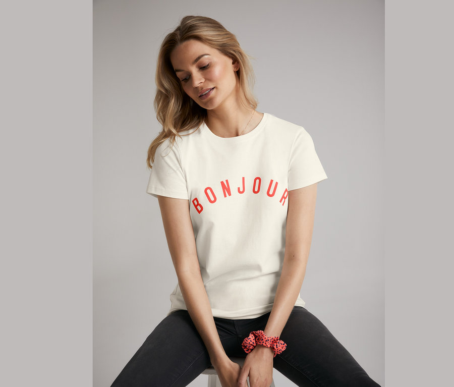 Frau sitzt auf einem Hocker und trägt eine Skinny-Jeans und ein T-Shirt mit Print.