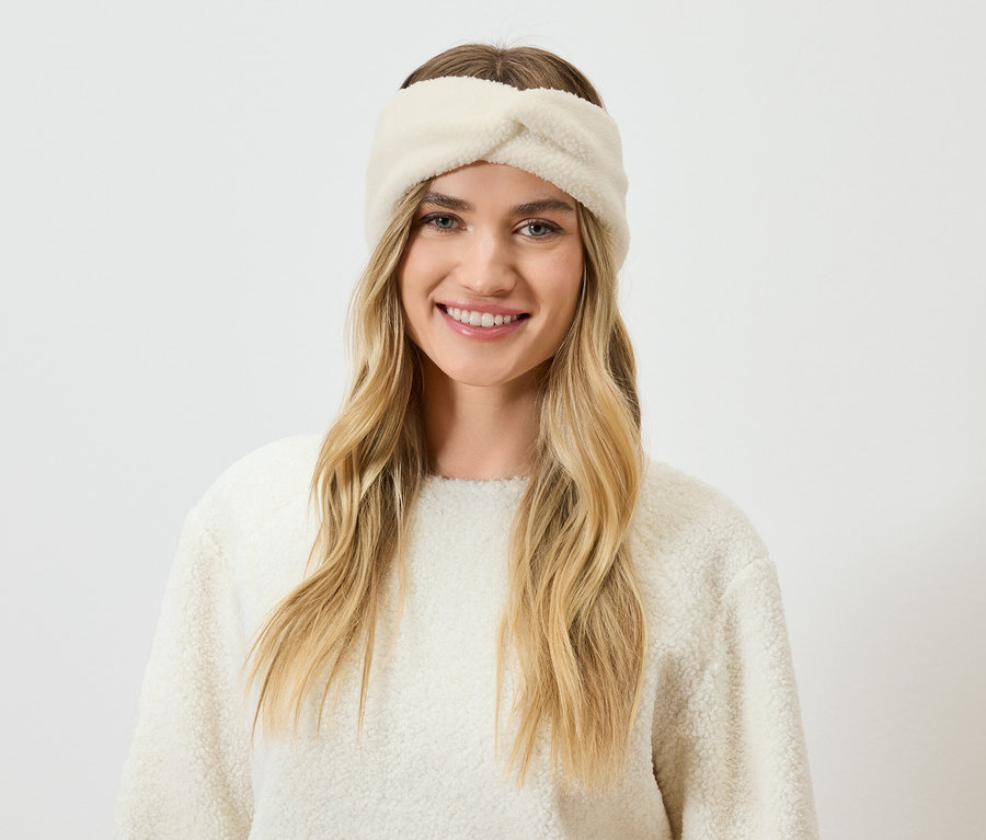 Porträt einer lächelnden Frau mit blonden Haaren, einem cremefarbenen Stirnband und Pullover.