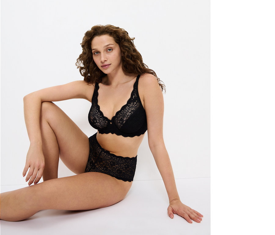 Frau sitzt auf dem Boden und trägt einen schwarzen Spitzen-BH und Höschen.