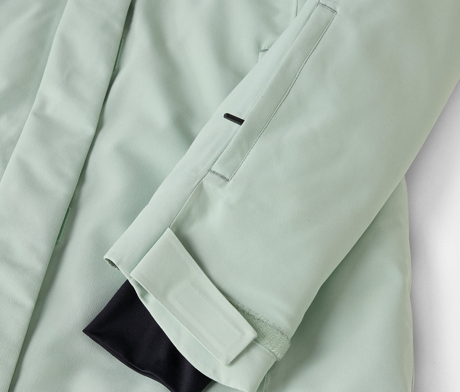 Detailaufnahme einer hellgrünen Jacke mit schwarzer Manschette und Ärmeltasche.