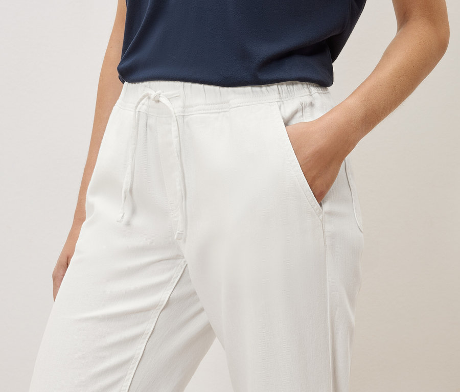 Eine Frau hat ihre Hand in der Tasche einer weißen Hose mit Gummibund und Kordelzug.