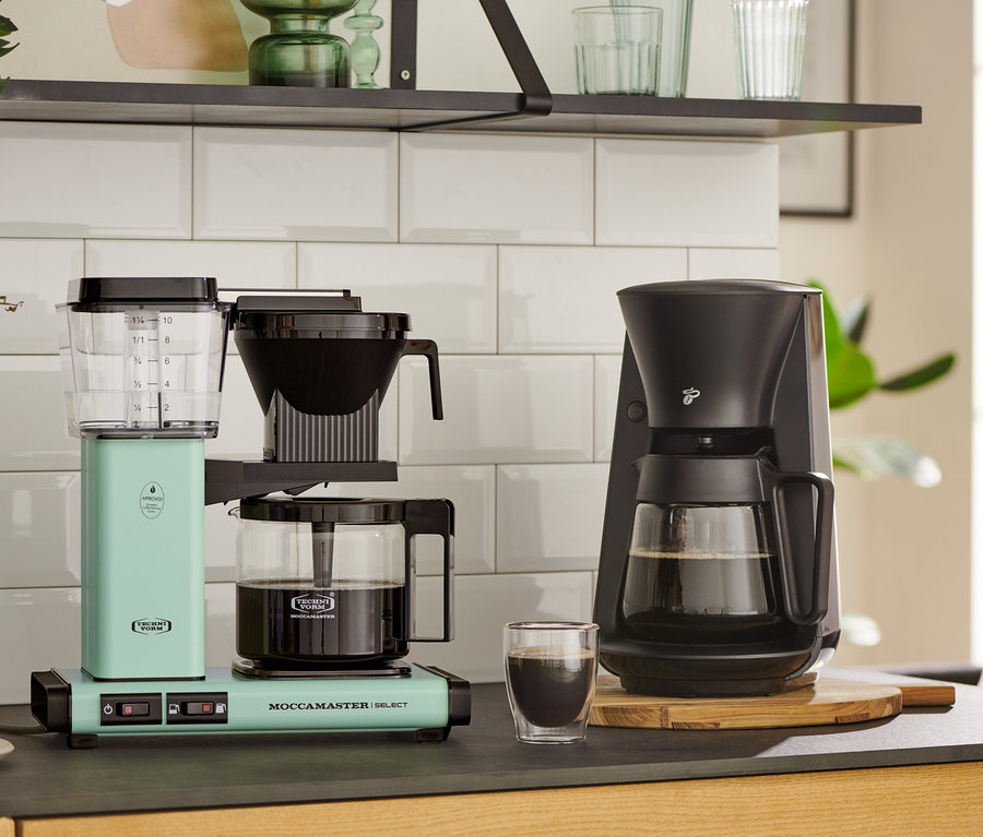 Zwei Kaffeemaschinen auf einer Küchentheke: eine pastellgrüne Moccamaster KBG Select Filterkaffeemaschine und eine schwarze.