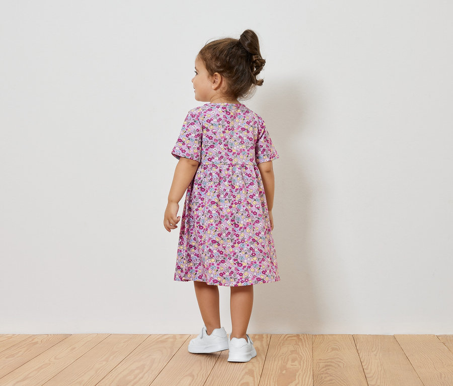 Mädchen im Blumenkleid und weißen Turnschuhen steht mit dem Rücken zur Kamera.