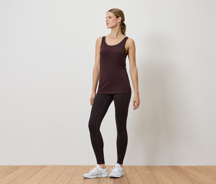 Frau in Tanktop und Leggings posiert im Innenbereich.