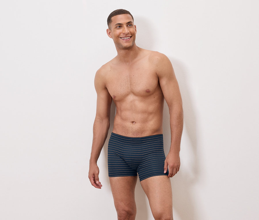 Ein barober Mann trägt blaue gestreifte Boxershorts und lächelt.