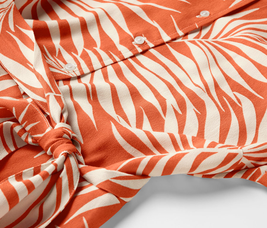 Detailansicht eines bedruckten Hemdblusenkleids mit Knöpfen und Taillenbindung.