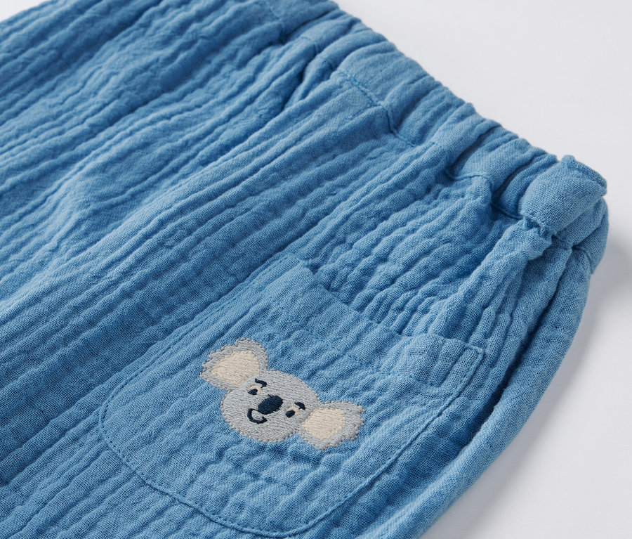 Detailaufnahme einer blauen Baby-Musselin-Schlupfhose mit Tasche und Koala-Stickerei.