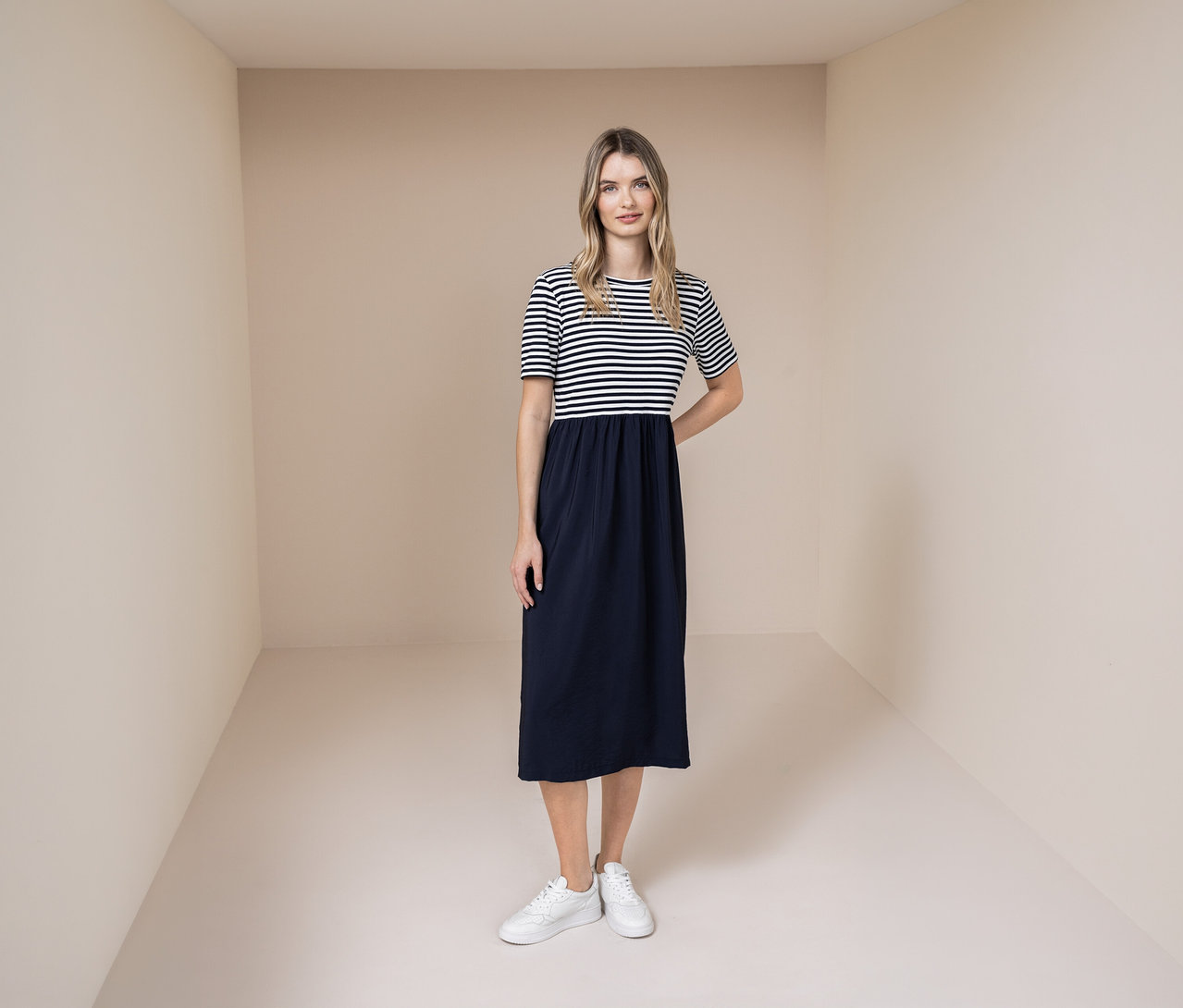 Frau mit Street One Kleid mit blau-weiß gestreiftem Oberteil und blauem Rock, dazu weiße Sneaker.