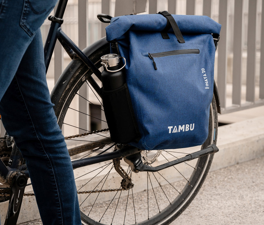 Person mit blauen Jeans steht neben einem Fahrrad mit einer blauen Tambu »INAYA« Fahrradtasche.
