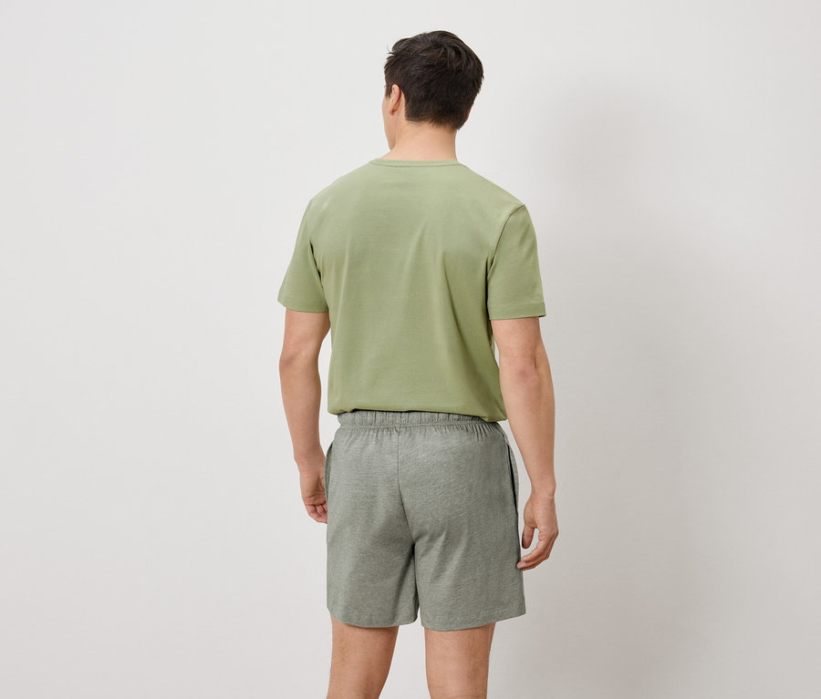 Ein Mann von hinten in einem olivgrünen T-Shirt und grauen Shorts.