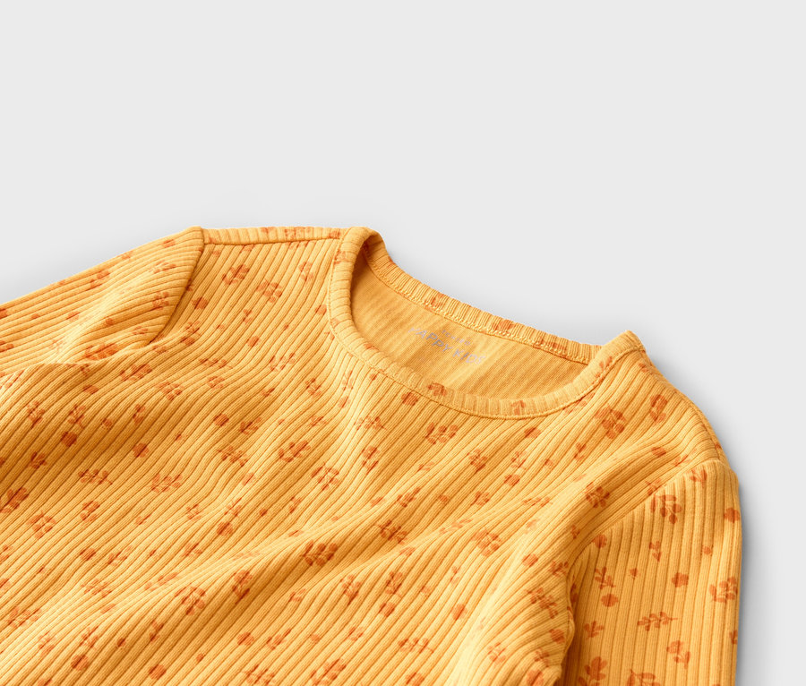 Nahaufnahme eines gelben, gerippten Langarmshirts mit orangefarbenem Blumenmuster vor einem grauen Hintergrund.