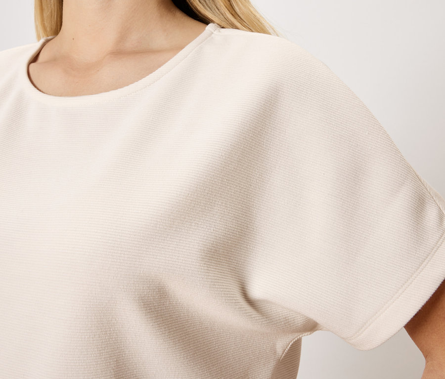 Nahaufnahme einer Frau, die ein kurzärmeliges, hellbeiges Oberteil mit Rundhalsausschnitt trägt.