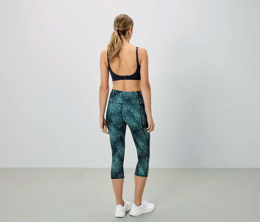 Frau von hinten, trägt Sport-BH und grüne Capri-Leggings mit Muster.