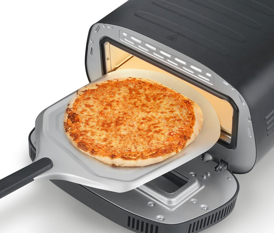Eine Pizza auf einem Pizzaschieber wird in einen schwarzen Ofen geschoben.