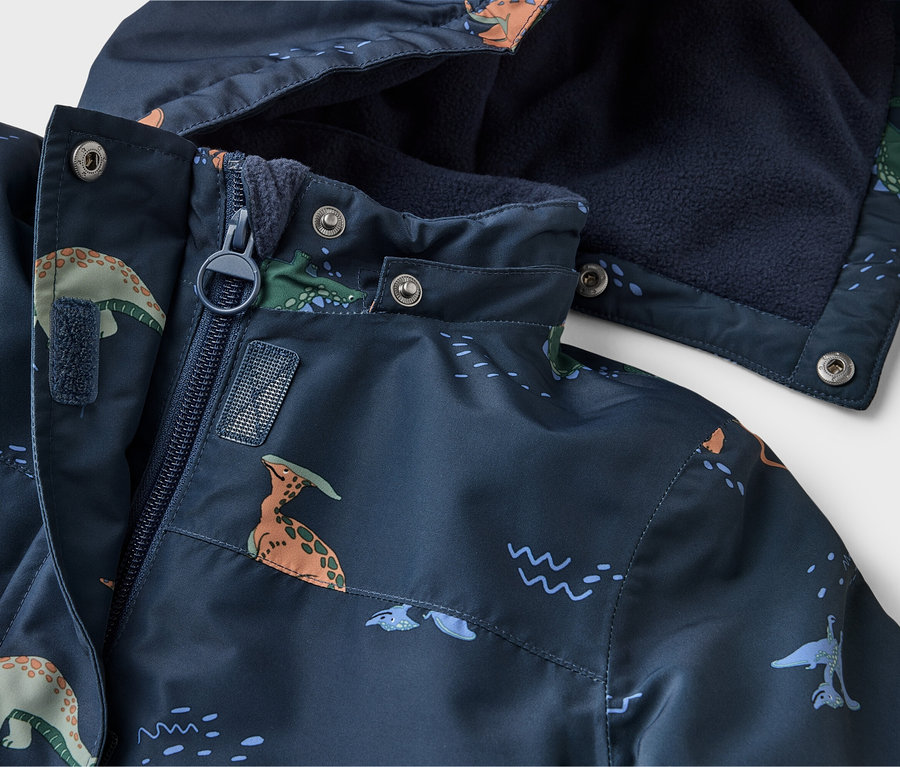 Nahaufnahme einer dunkelblauen Jacke mit Dinosaurier-Muster, Reißverschluss und Kapuze mit marineblauem Fleecefutter.