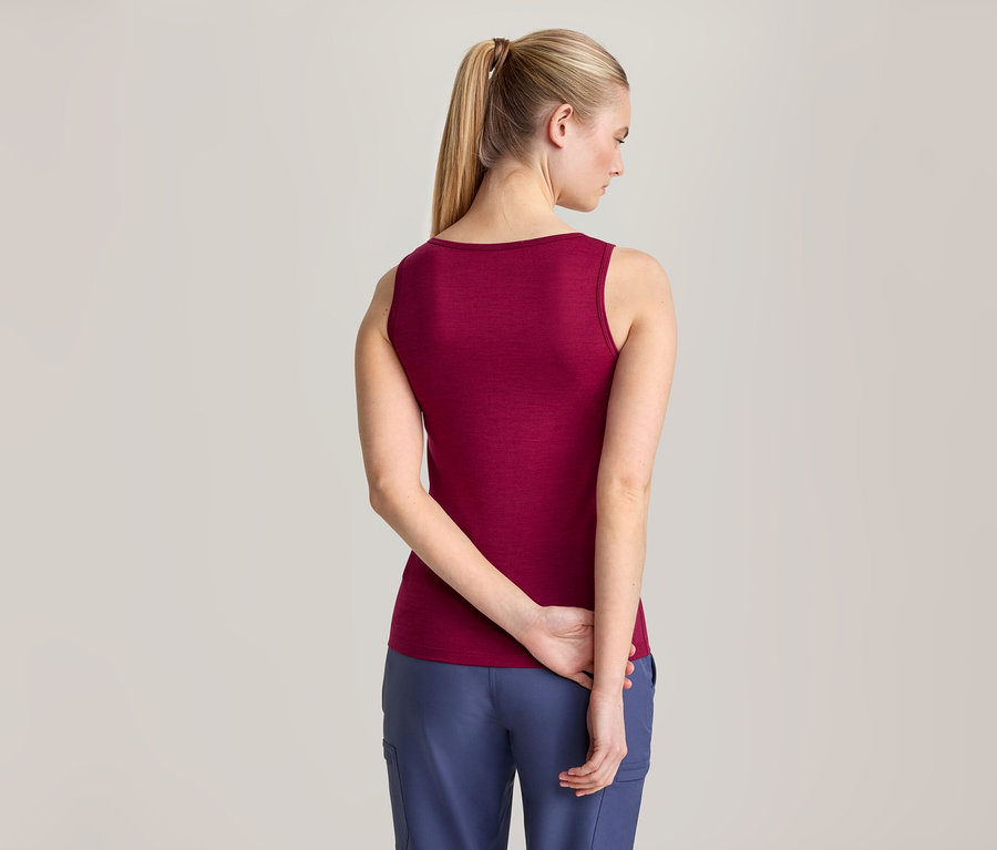 Frau von hinten in weinrotem Tanktop und blauer Hose, die Hände hinter dem Rücken verschränkt.