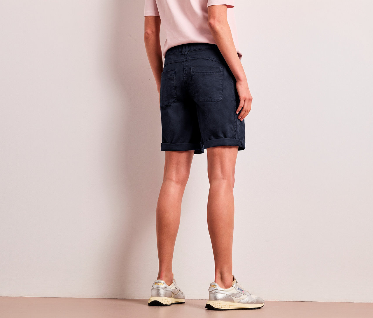 Eine Person von hinten trägt ein hellrosa T-Shirt, navyfarbene Street One Bermuda »Yulius« und silberne Sneaker.