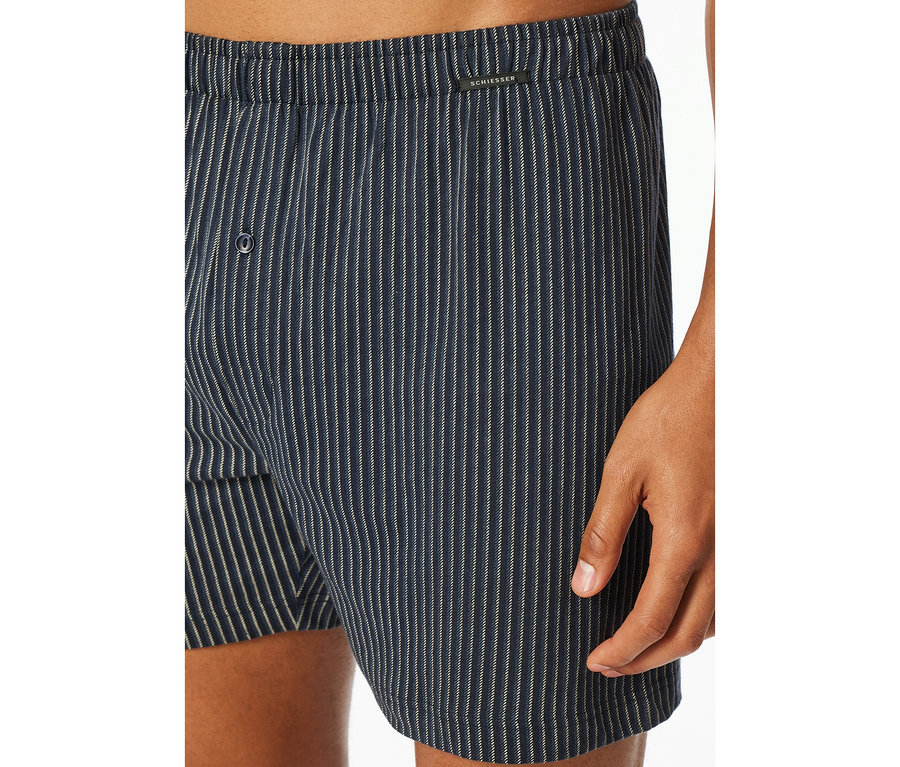 Nahaufnahme einer Person in blau-weiß gestreiften SCHIESSER Jersey-Boxershorts mit Knopfleiste.