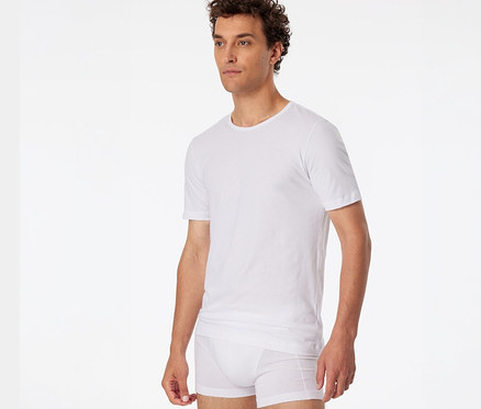 Mann mit lockigem Haar trägt ein weißes SCHIESSER T-Shirt und weiße Boxershorts.