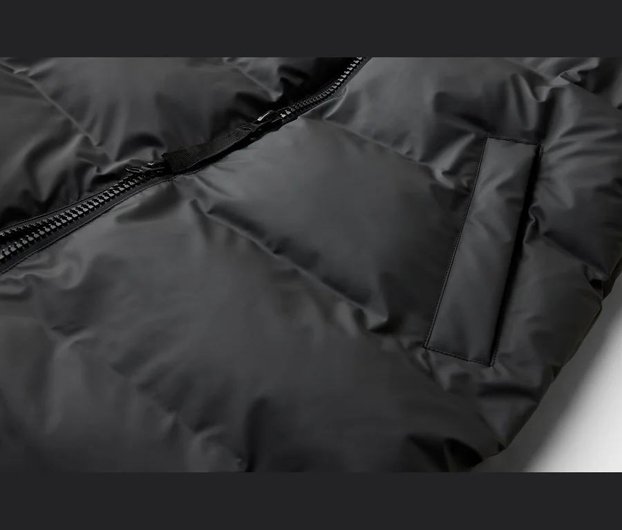 Nahaufnahme einer schwarzen Steppjacke mit sichtbarem Reißverschluss und einer vertikalen Tasche.
